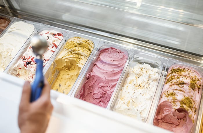 hand holding ice cream scoop over retail gelato case