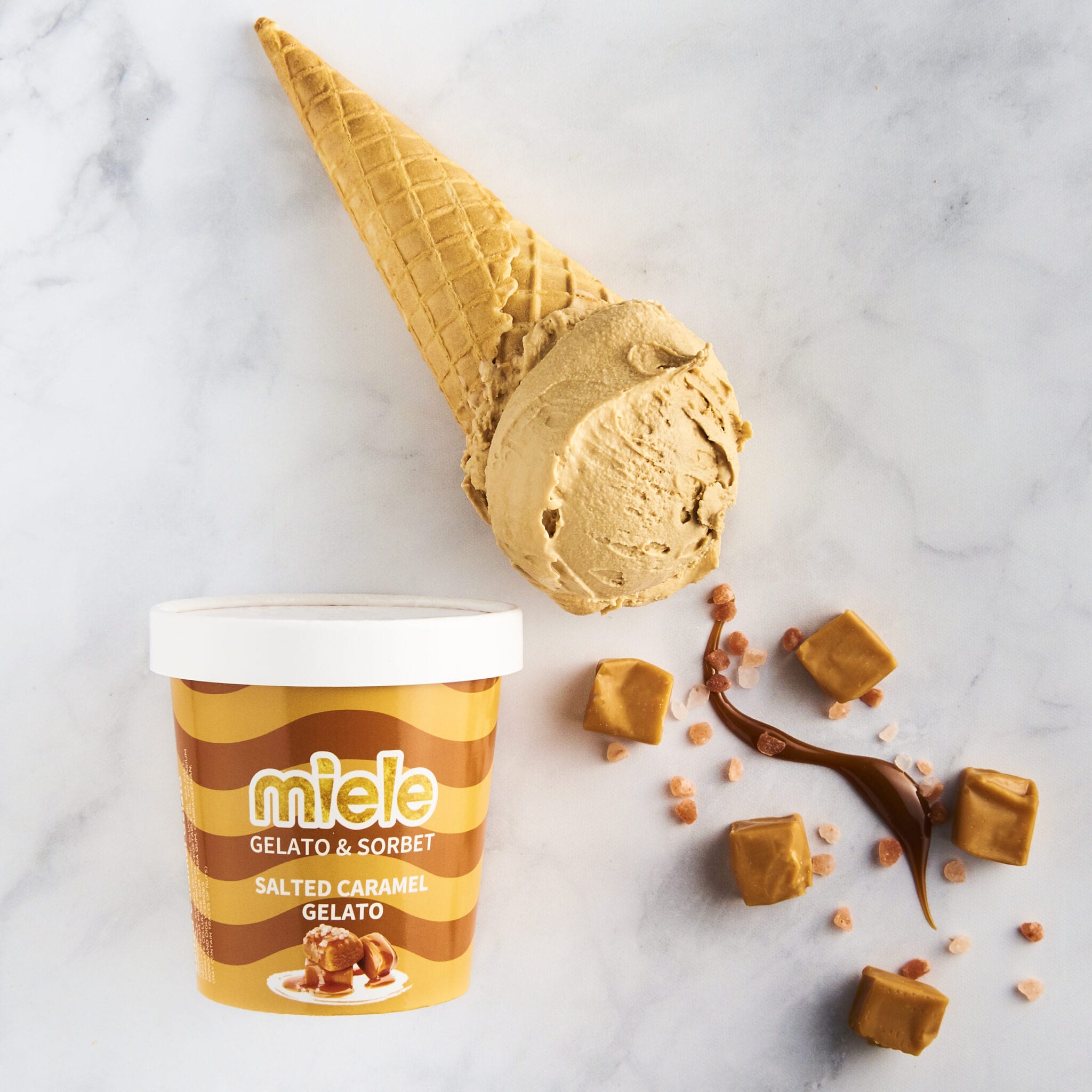 pint of miele salted caramel gelato next to waffle cone with gelato and caramel pieces